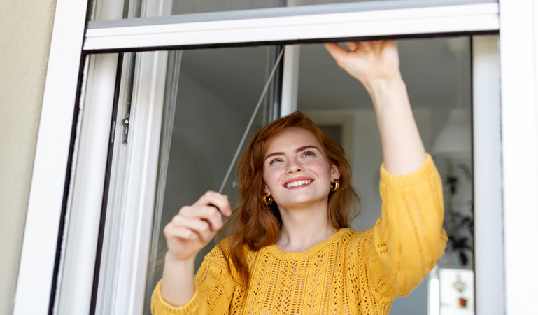 mujer bajando mosquitera en una ventana